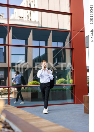 Ginger bearded man walking outdoors in business district speaking on mobile phone 130159545