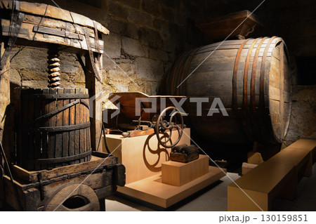 A historic wine cellar with an antique wooden press, grape crusher, and giant barrel. The concept is traditional winemaking heritage and craftsmanship. 130159851