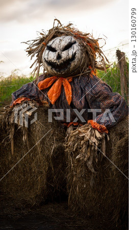 Creepy scarecrow sitting on hay bales at dusk 130160799