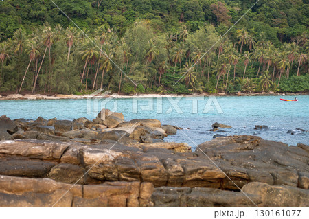 Rocky shoreline with tropical forest and boat on calm sea water 130161077