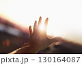 A strong, brilliant beam of light shining through the arms and fingers stretched out toward the bright sun. 130164087