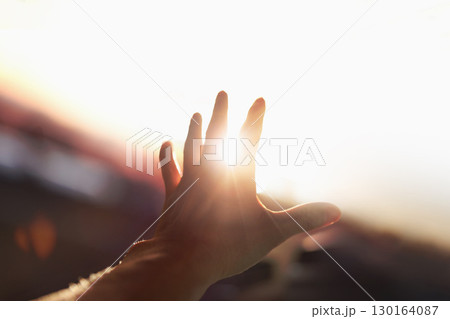 A strong, brilliant beam of light shining through the arms and fingers stretched out toward the bright sun. 130164087