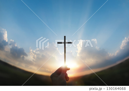 A hand holding the cross of Jesus Christ toward the rising sun, a background of faith, hope, and the New Year. A hand holding the cross of Jesus Christ toward the rising sun, a background of faith, hope, and the New Year. 130164088