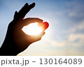 A silhouette of a woman holding a red heart, a symbol of precious life and love, against a blue sky and bright sunlight background. 130164089