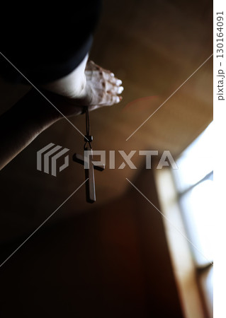 The hands of a Christian holding the cross of Jesus Christ in a church and praying with both hands together 130164091