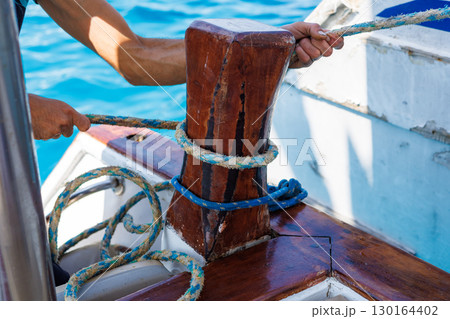 Sailor securing rope on wooden cleat Sailor securing rope on wooden cleat 130164402