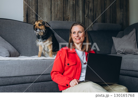 Smiling woman with dog filming on smartphone at home. Remote work, freelance lifestyle, online education with pet companion in cozy interior. Smiling woman with dog filming on smartphone at home. Remote work, freelance lifestyle, online education with pet companion in cozy interior. 130165768