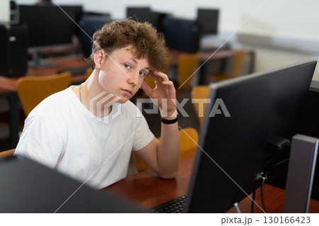 Focused puzzled teenage boy studying in computer lab 130166423