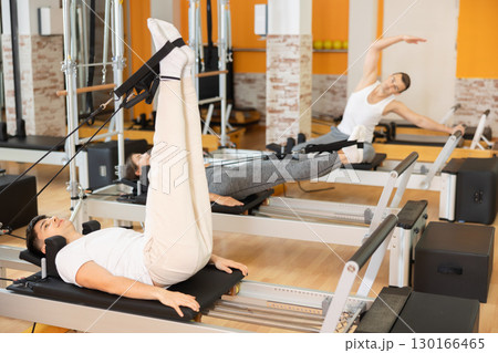 Guy performing rehabilitation feet-in-strap exercises on Pilates reformer 130166465