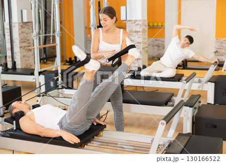 Man athlete performs exercises to increase leg strength using sling reformer under coach guidance. 130166522