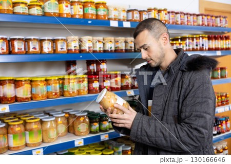 In Russian goods store, man choose jar of pickled fermented cabbage 130166646