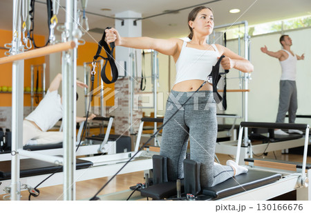 Girl performing pulling straps exercise on Pilates reformer Girl performing pulling straps exercise on Pilates reformer 130166676