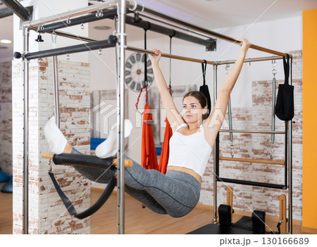 Sporty girl hanging on trapeze table at Pilates workout Sporty girl hanging on trapeze table at Pilates workout 130166689