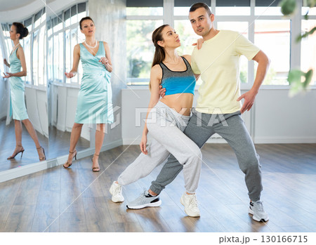 Couple rehearsing elegant tango under guidance of female teacher 130166715