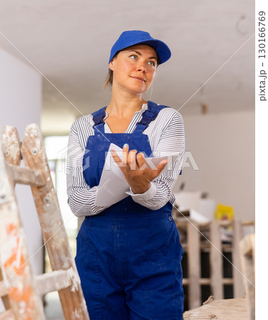 Cheerful young woman builder checking project documentation Cheerful young woman builder checking project documentation 130166769