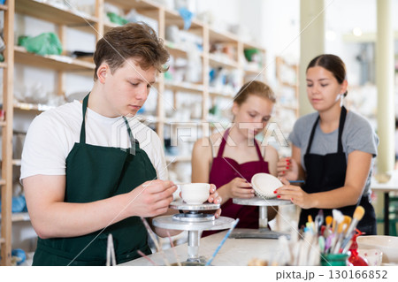 Young man leveling the edges of pottery with wooden stick 130166852