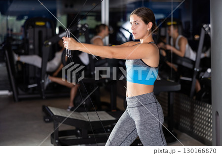 Sportive young girl training her arms on adjustable cable exercise machine in gym 130166870