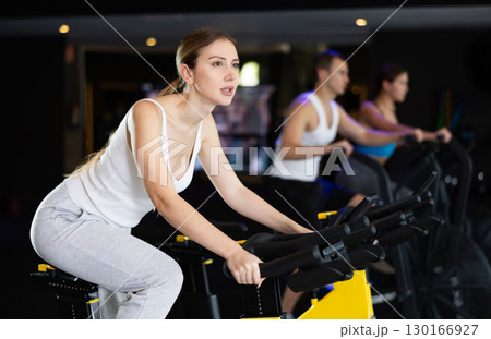 Sportive young girl doing spin bike exercises in well-equipped gym Sportive young girl doing spin bike exercises in well-equipped gym 130166927