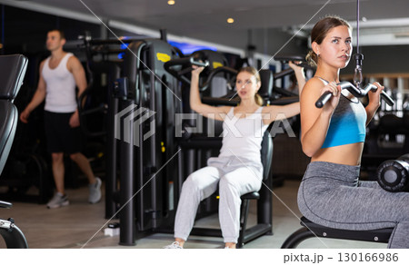 Slender athletic girl work out muscles of arms and shoulders on simulator in gym of fitness club 130166986