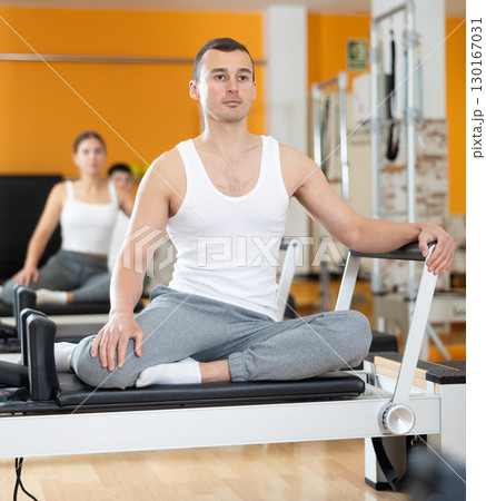 Man sits on reformer and rests while doing exercises for muscles of body and torso. 130167031