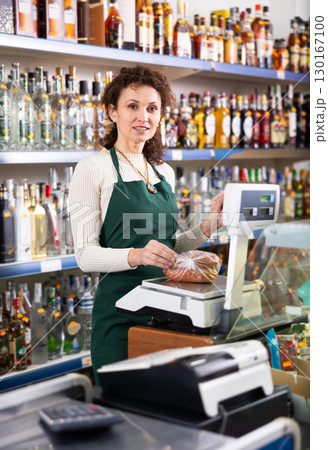 Andult saleswoman weighs sausages on scale 130167100