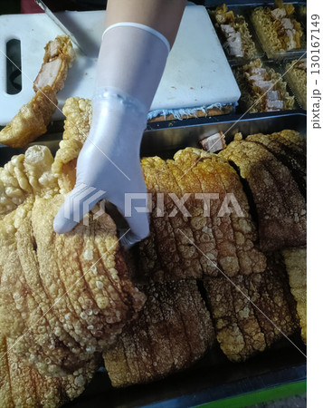 Person wearing white glove handling fried pork belly food stall, with crispy, golden brown pork pieces displayed tray, ready for sale or serving 130167149