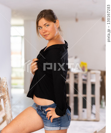 Woman in shorts and black shirt with naked tummy coquettishly posing in room during renovation Woman in shorts and black shirt with naked tummy coquettishly posing in room during renovation 130167283