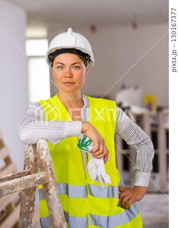 Sexy young woman in a yellow vest and protective helmet poses playfully in renovated room Sexy young woman in a yellow vest and protective helmet poses playfully in renovated room 130167377