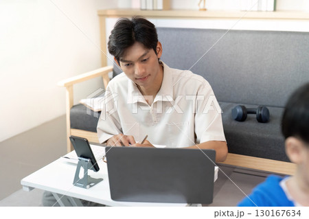 Remote work. Young man studying with laptop and taking notes in a cozy home environment. 130167634