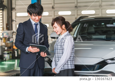 整備工場のピットにある車の前でタブレットを見るセールスマンの男性と女性事務員 130167823