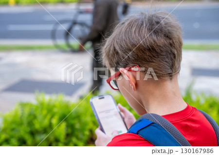 Boy using smartphone while walking near the street in a busy urban area during the afternoon Boy using smartphone while walking near the street in a busy urban area during the afternoon 130167986
