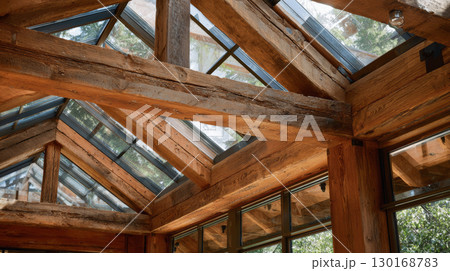 Rustic wooden beams and glass ceiling create warm, natural atmosphere in this bright, cozy interior with forest views outside windows 130168783