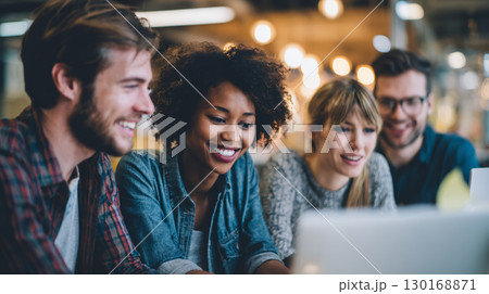 Multicultural team collaborating in modern office space smiling and working together on laptop with warm lighting and creative atmosphere 130168871
