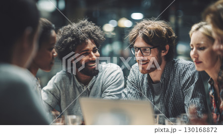 Multicultural team collaborating in modern office space with laptop, sharing ideas and smiling during work meeting 130168872