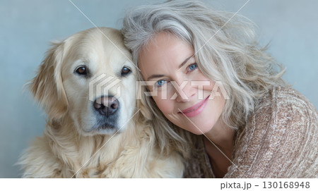 Mature woman with gray hair smiling and leaning close to golden retriever dog, showing affection and warmth in cozy setting 130168948