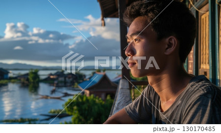 young man contemplating lakeside village at sunset 130170485