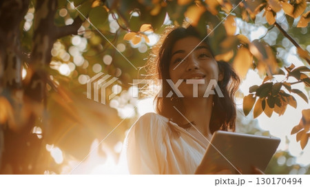 woman reading tablet under tree sunlight 130170494