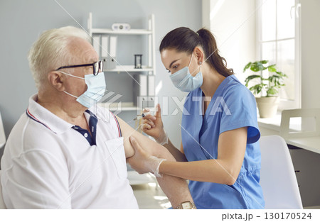 Old man in medical face mask gets injection Covid-19 vaccine at hospital in immunization campaign. 130170524