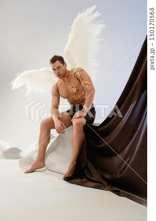 Model with angel wings and artistic body adornments poses against backdrop 130170568