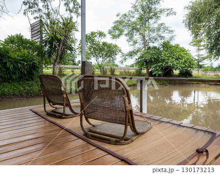 Rattan Chair on Mat on Wooden Deck by Small Pond. Rattan Chair on Mat on Wooden Deck by Small Pond. 130173213