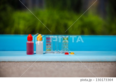 Pool water test kit with chemical dropper bottles and color comparator, used for swimming pool maintenance, placed on the edge in sunlight. 130173364