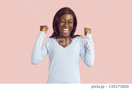 Young funny girl do winner gesture clenching fists celebrating success on pink background. 130173800