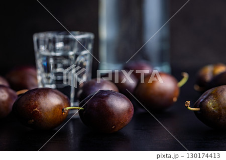 Plums and distilled alcohol on black table. Plum brandy shot. 130174413