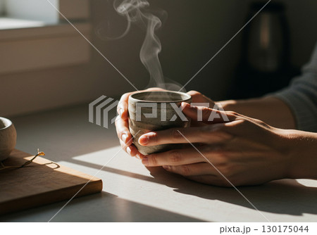 Womans Hands Holding a Steaming Cup of Tea 130175044