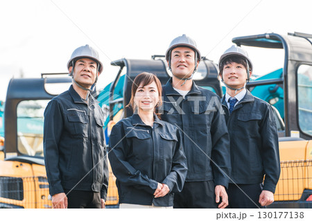 重機の前にいる作業着姿の建設業・建築業の作業員男女 130177138