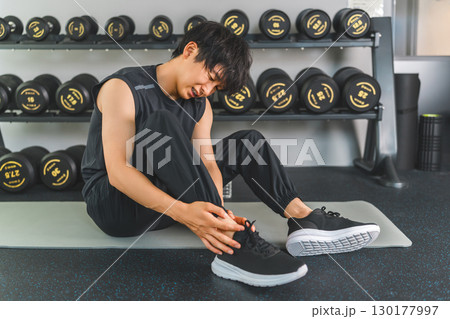 スポーツジムで足首を痛めるスポーツウェア姿の若いアジア人男性 130177997