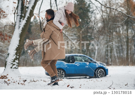 Playful mood. Happy couple having a walk in winter forest. Blue car is parked Playful mood. Happy couple having a walk in winter forest. Blue car is parked 130178018