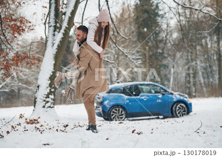 Playful mood. Happy couple having a walk in winter forest. Blue car is parked Playful mood. Happy couple having a walk in winter forest. Blue car is parked 130178019