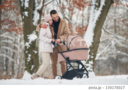 Mother and father with pram. Lovely couple have a walk in the winter forest Mother and father with pram. Lovely couple have a walk in the winter forest 130178027