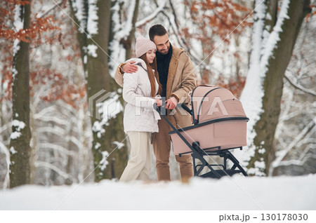 Parents are standing with pram. Lovely couple have a walk in the winter forest Parents are standing with pram. Lovely couple have a walk in the winter forest 130178030
